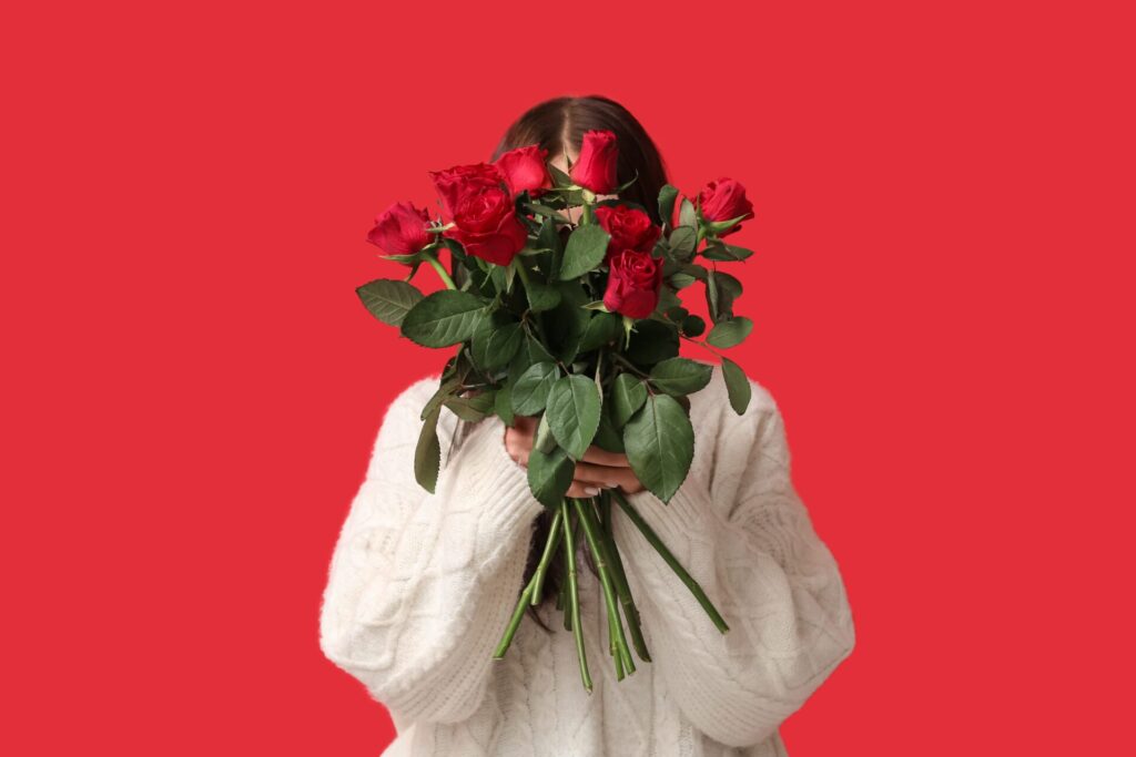 Young,Woman,With,Bouquet,Of,Beautiful,Red,Roses,On,Color